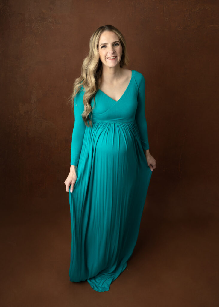 mom wearing green maternity gown on a brown backdrop