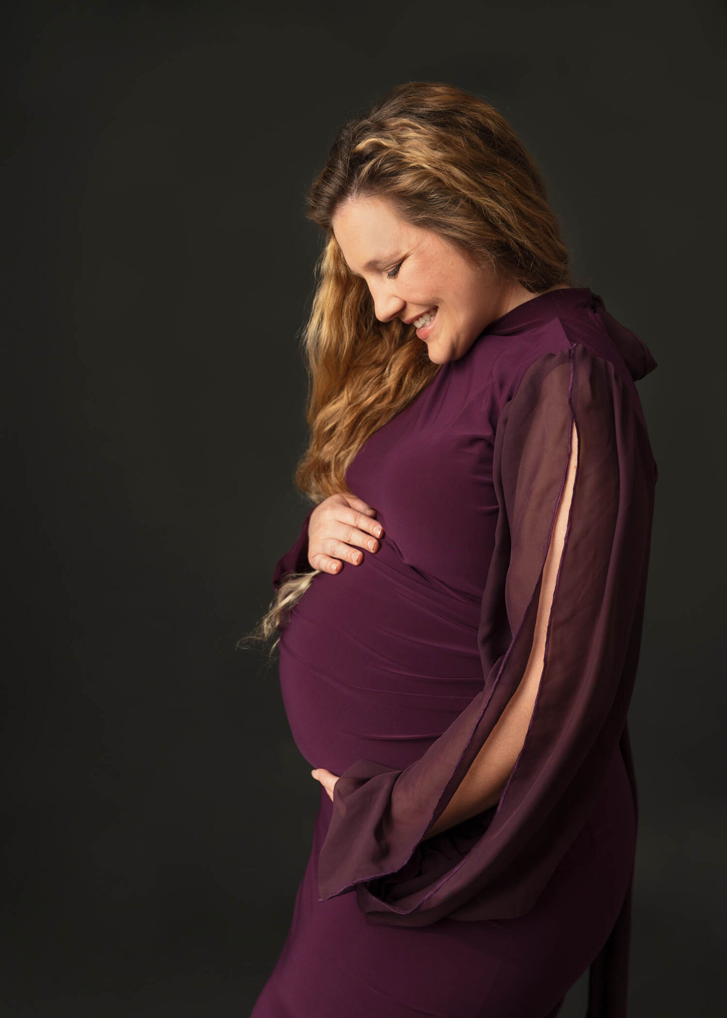 pregnant mom holding belly and smiling down wearing purple maternity gown