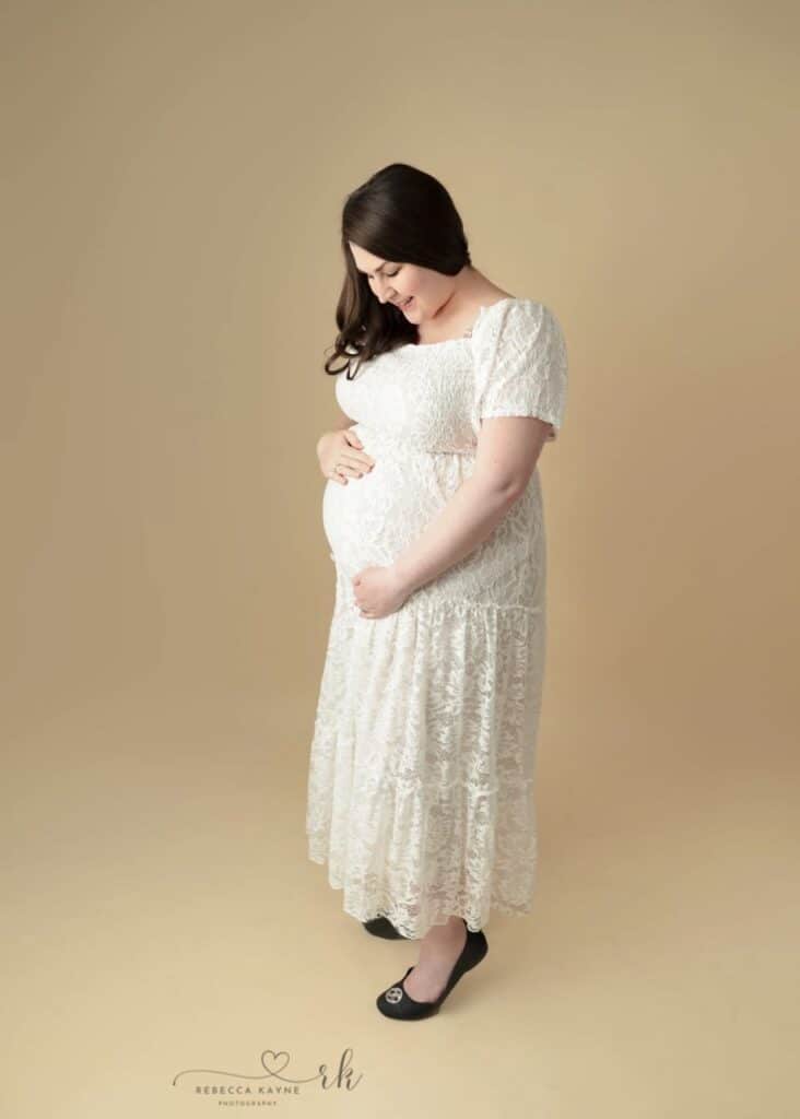 woman in white maternity dress looking down at baby bump