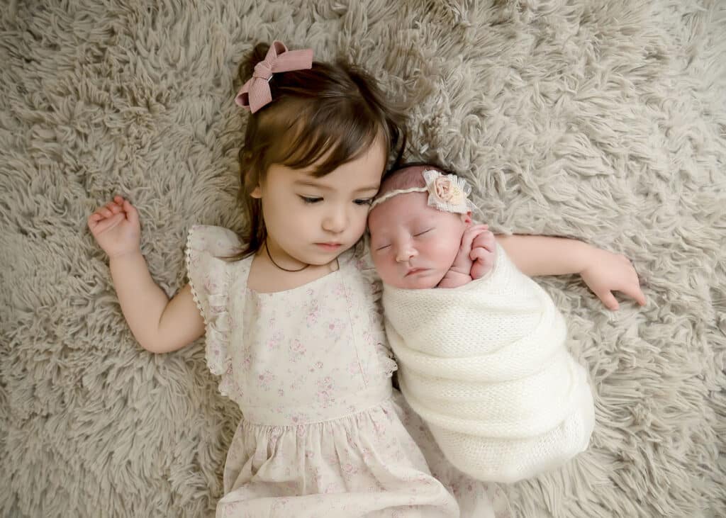 utah county newborn studio toddler and newborn baby sister snuggling on tan blanket