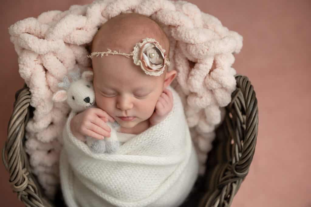 baby snuggling white deer on pink blanket