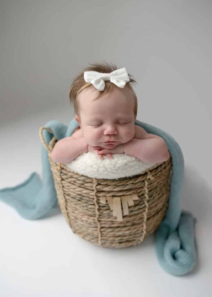 baby girl in white headband and blue wrap sitting in basket