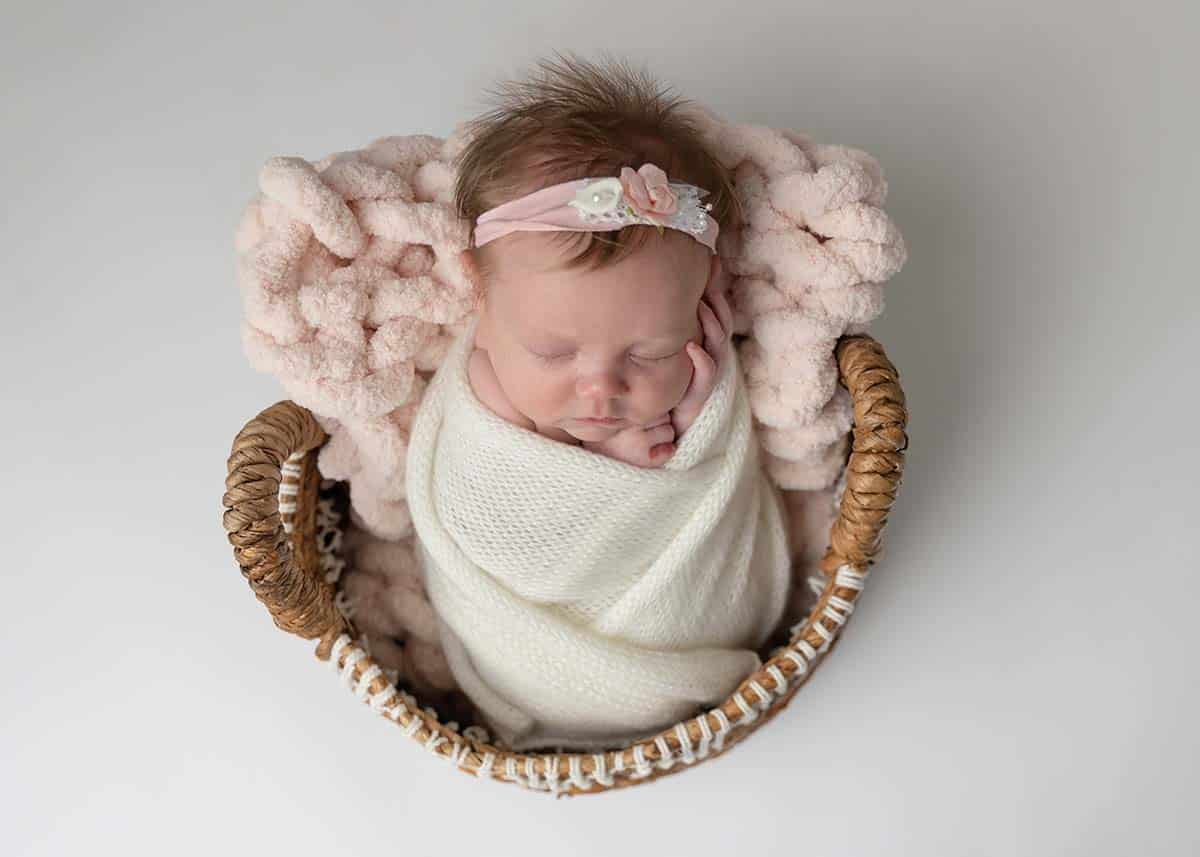 newborn baby girl wrapped in white wrap on pink blanket in basket