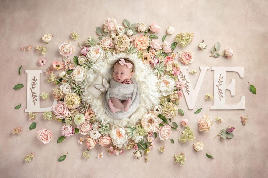 newborn baby girl in white fur surrounded by flowers and letters spelling love