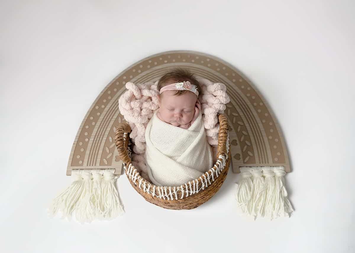 rainbow baby in a basket with wooden boho rainbow surrounding