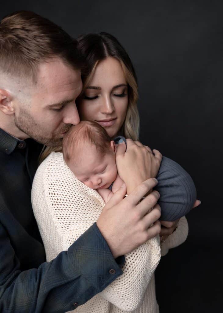 mom and dad with baby dad kissing babys head