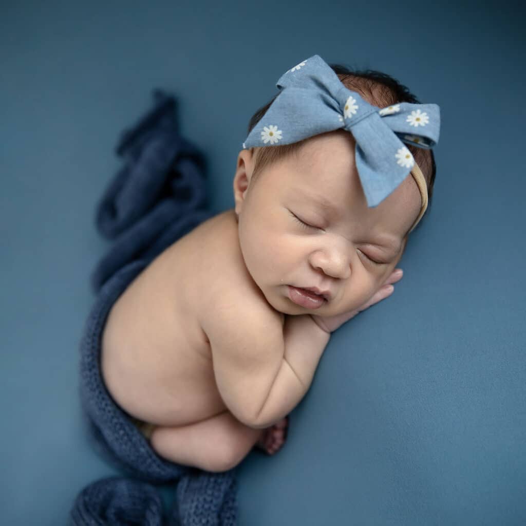 newborn baby girl in blue bow on blue blanket
