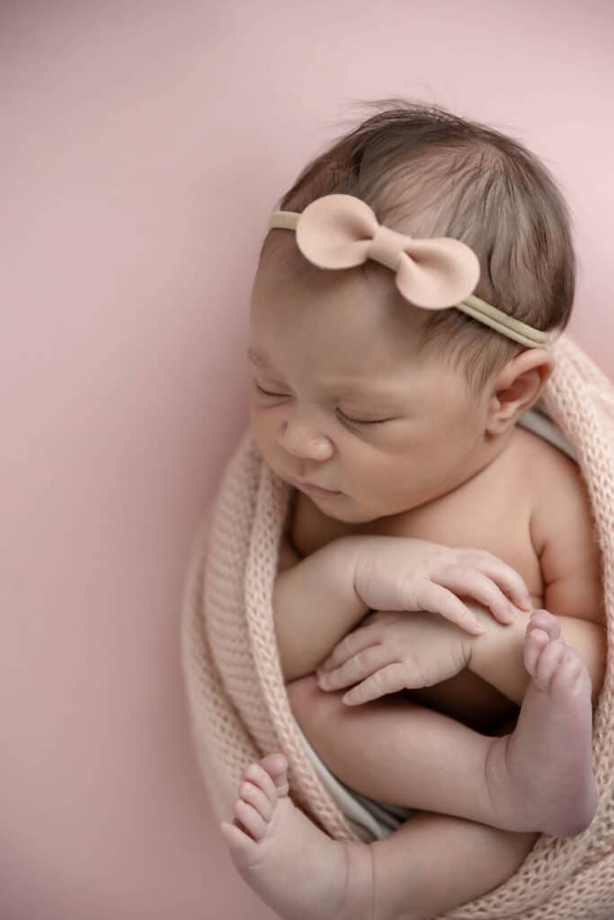 newborn baby girl in pink bow on pink blanket