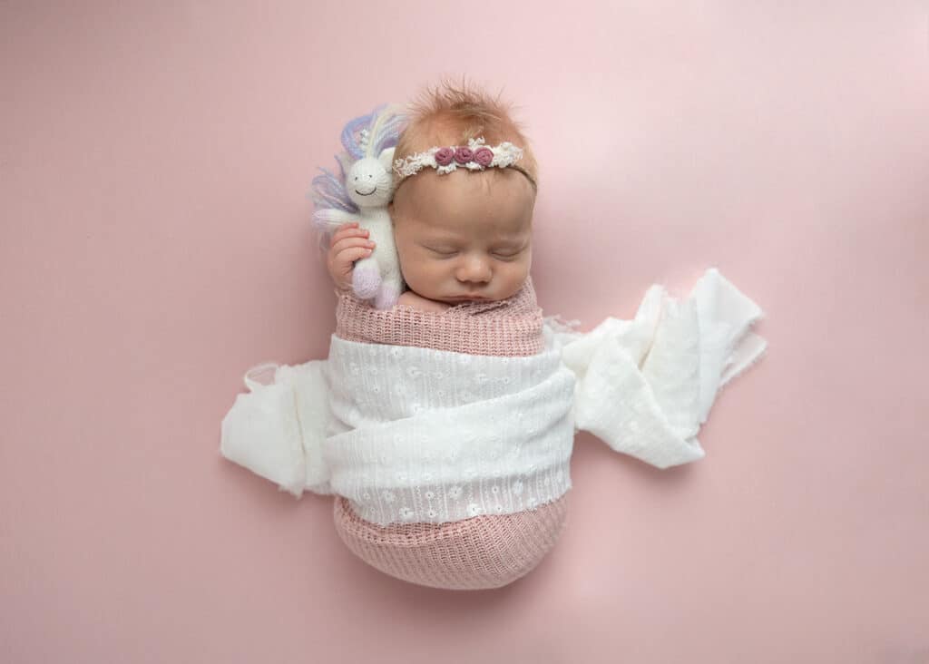 newborn baby girl holding unicorn on pink blanket
