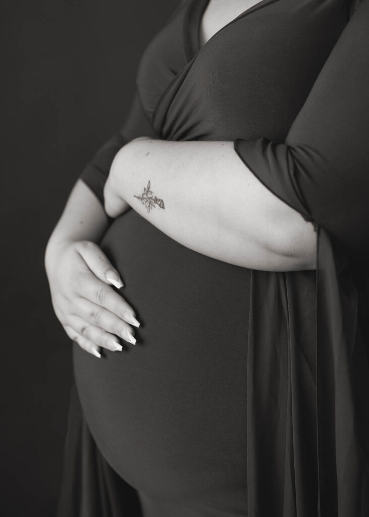 pregnant mom holding belly bump flower tattoo on arm