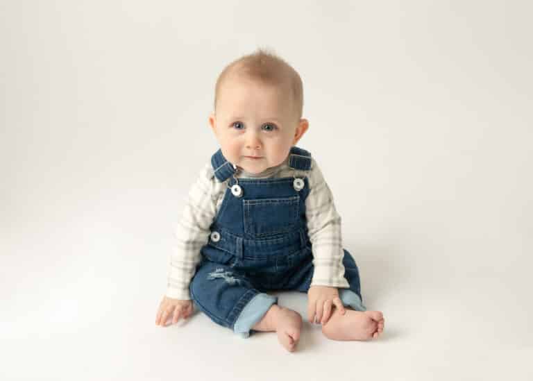 cute baby in overalls sitting on a white backdrop