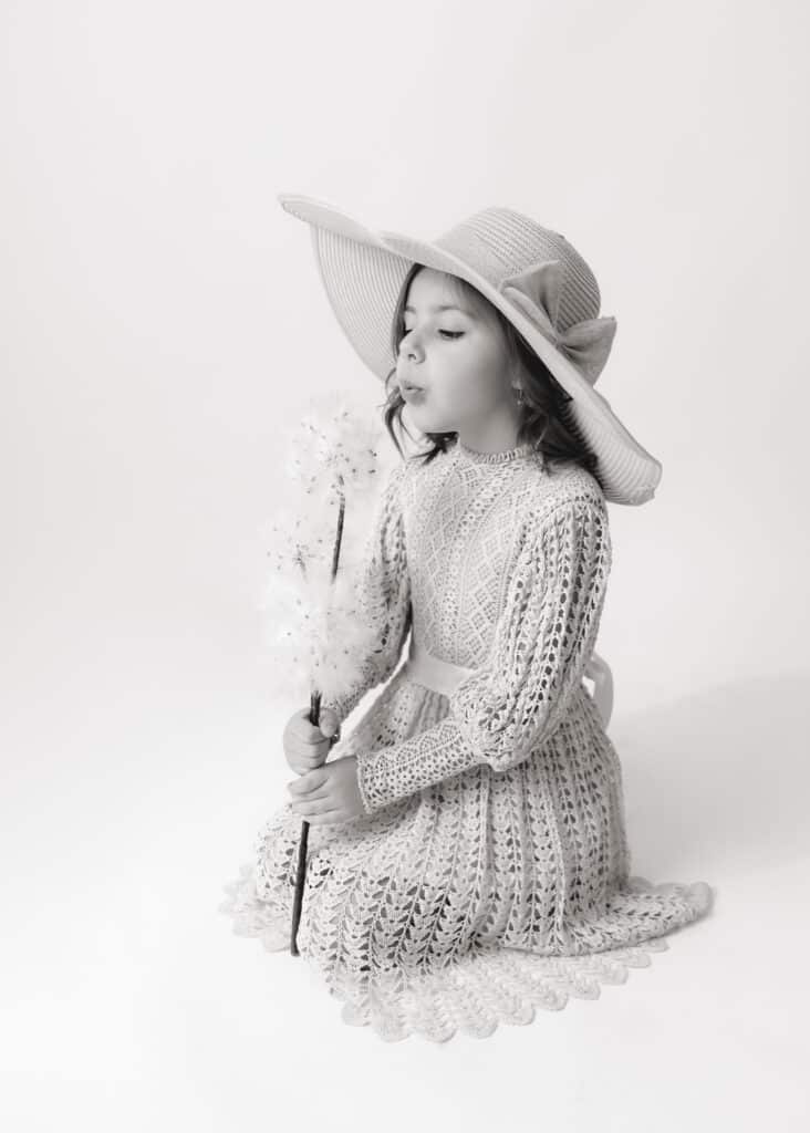 black and white portrait of little girl in a sunhat blowing dandelion seeds in a utah county portrait studio