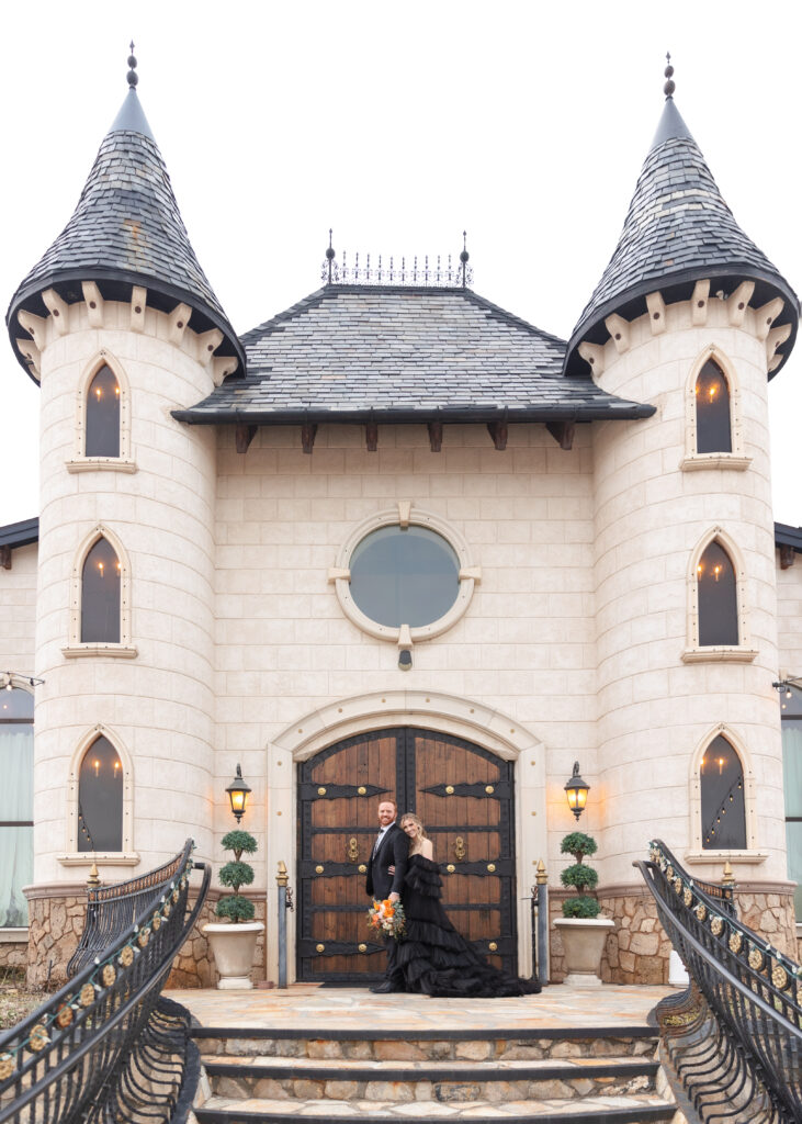 bride and groom wearing black in front of a castle