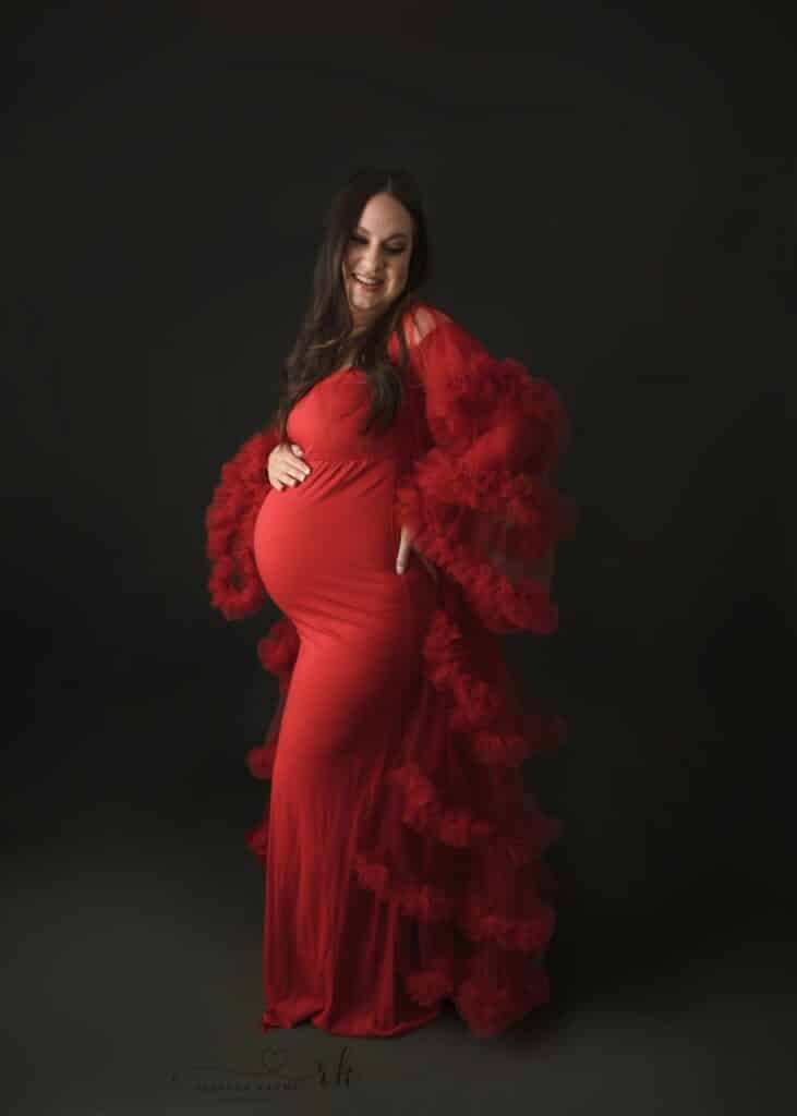 mom in red flowing maternity gown looking back over her shoulder