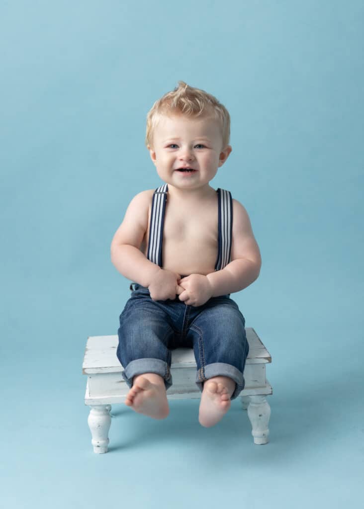 baby sitting on white stool on blue background during cake smash session