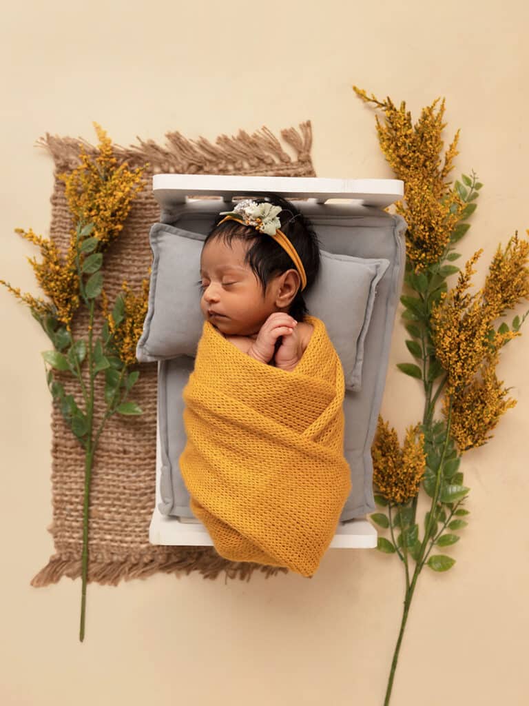 newborn baby girl in a yellow wrap near yellow flowers taken by a utah county photographer Rebecca Kayne Photography