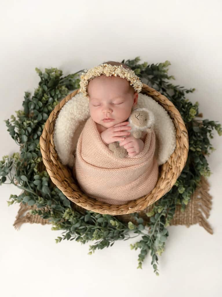 newborn portrait of baby girl holding lamb lovey in a basket surrounded by greenery taken by a utah county newborn photographer