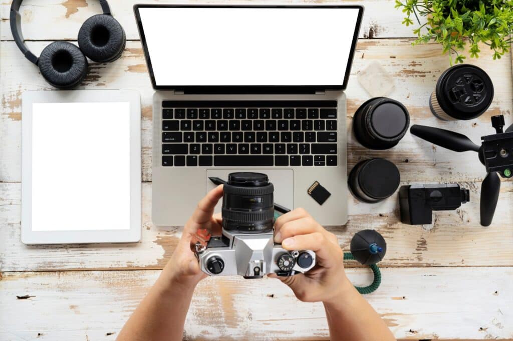 person holding camera next to computer and laptop editing tutorials