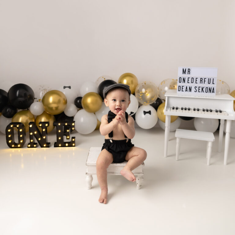 what is a cake smash session boy with black and gold balloon arch and baby piano