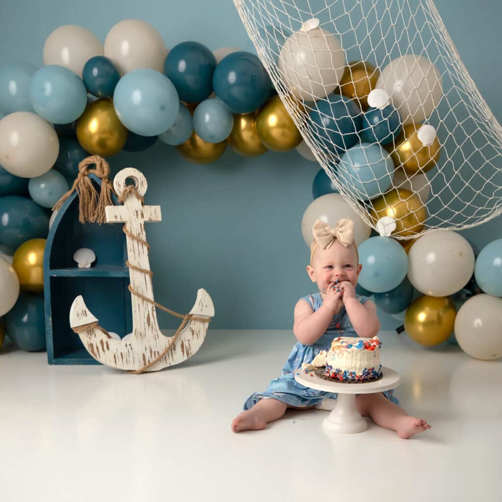 what is a cake smash session cute girl smiling on a nautical backdrop with blue balloon arch