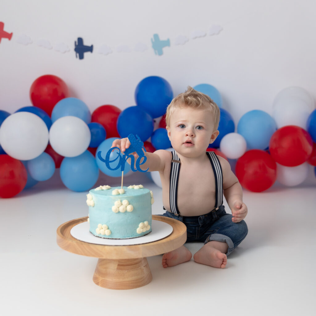 what is a cake smash session baby boy in front of airplane backdrop with cute cloud cake